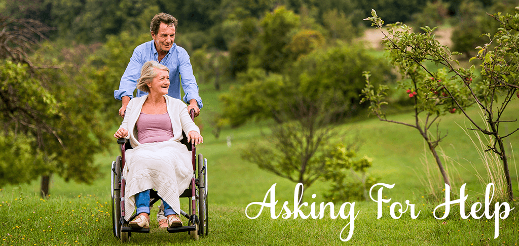 Asking For Help: a man pushes a smiling older woman in a wheelchair across a grassy hill