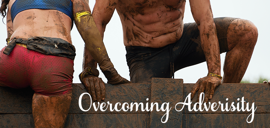 Overcoming Adversity: two mud-covered athletes climb over a wooden wall in an obstacle race